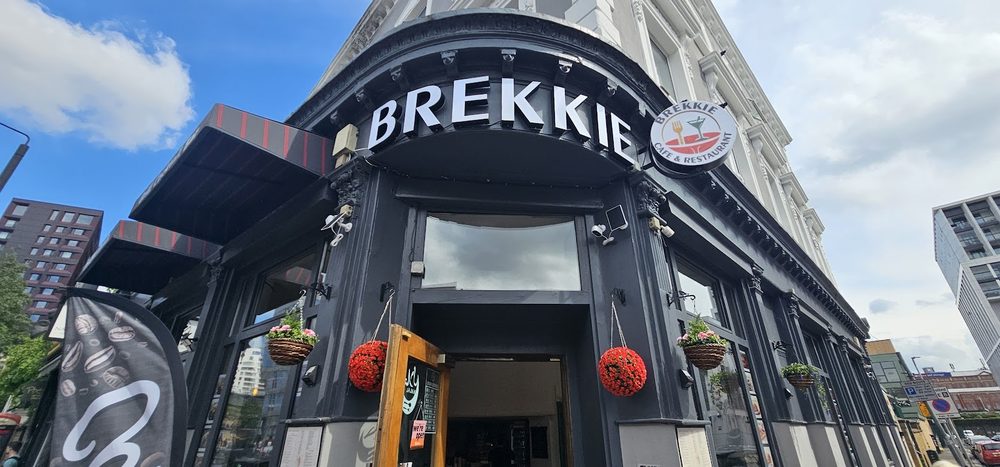 The dark corner shopfront of Brekkie on Battersea Park Road, arched entrance under a blue sky